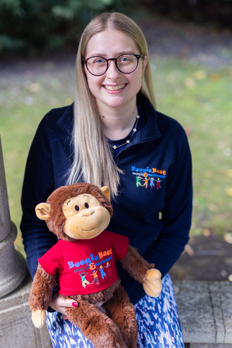 caitlin, long blonde hair and navy top holding a giggles the monkey