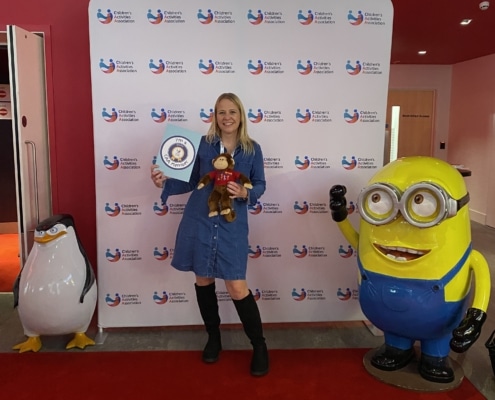 lady with long blonde hair holding a monkey and a CAA member board next to a minion and a penguin