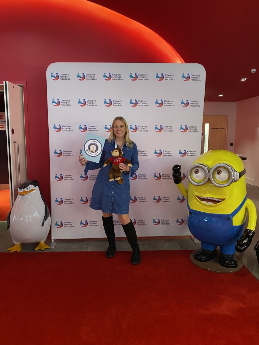 lady with long blonde hair holding a monkey and a CAA member board next to a minion and a penguin
