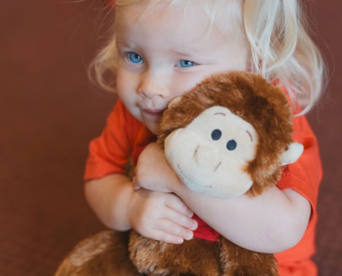 Girl with blonde hair wearing a red tshirt cuddling a monkey