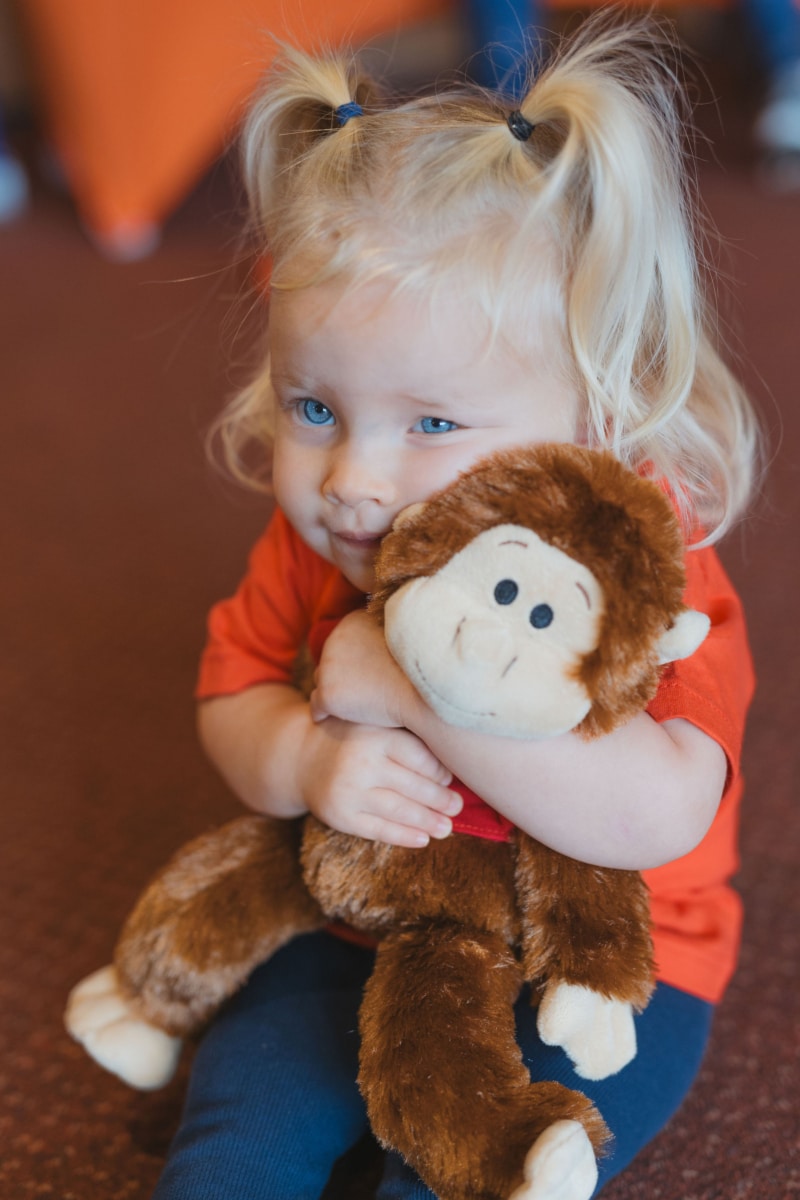 Girl with blonde hair wearing a red tshirt cuddling a monkey