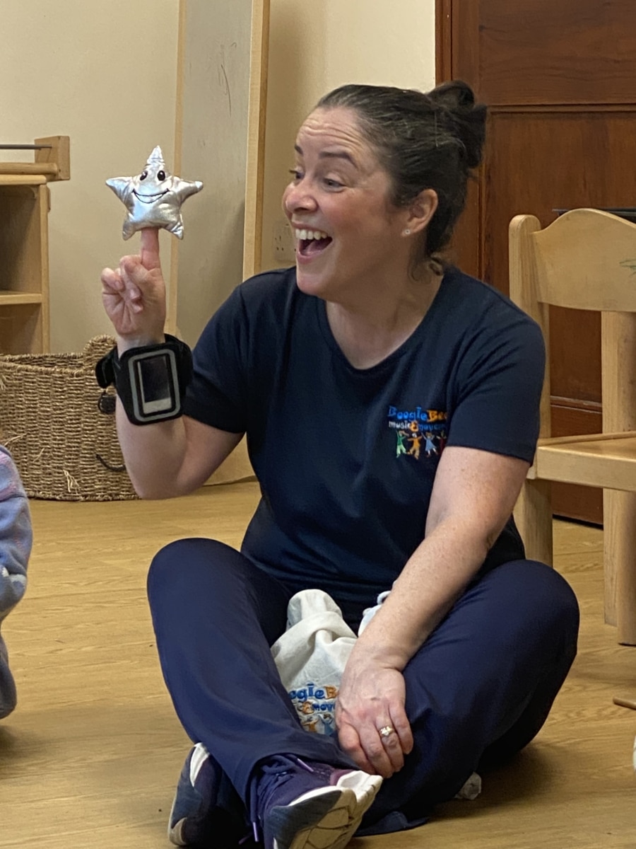 lady with brown hair tied back holding a star and singing